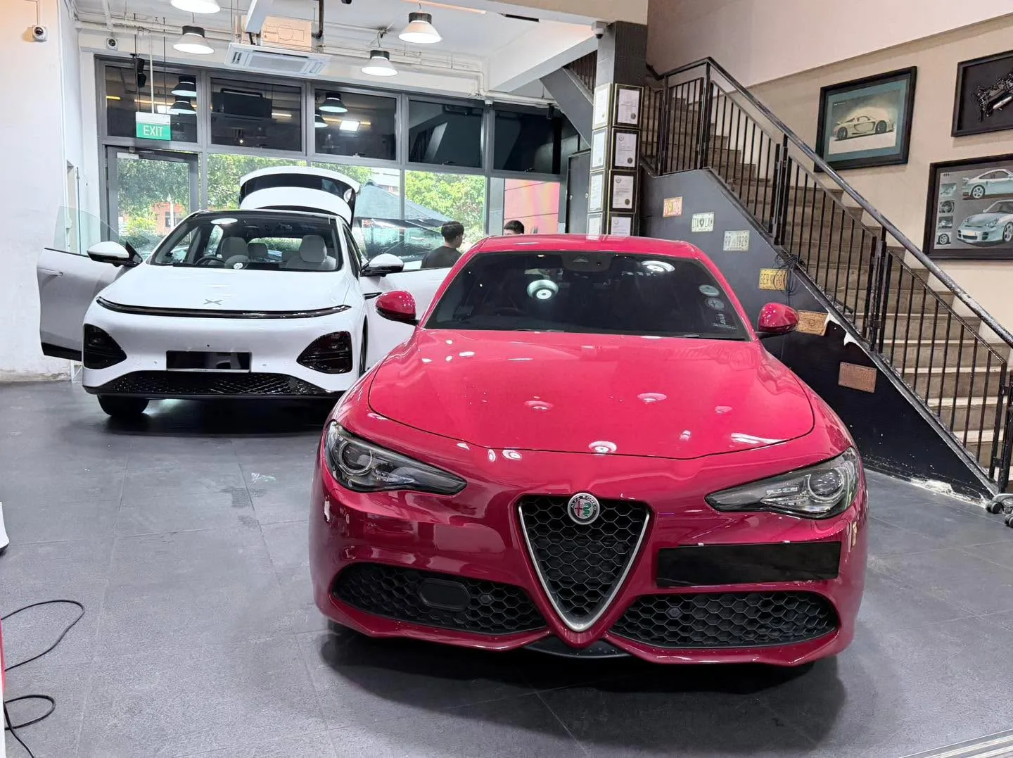 A red Alfa Romeo Giulia in the foreground with a white hatchback behind it.