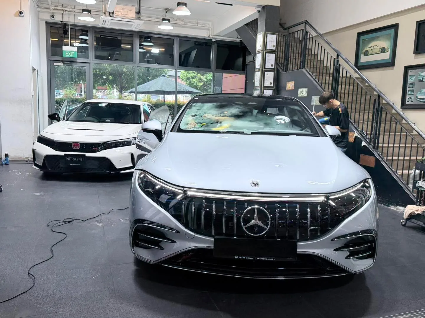 A silver Mercedes-Benz and a white Honda Civic with doors open inside the workshop.