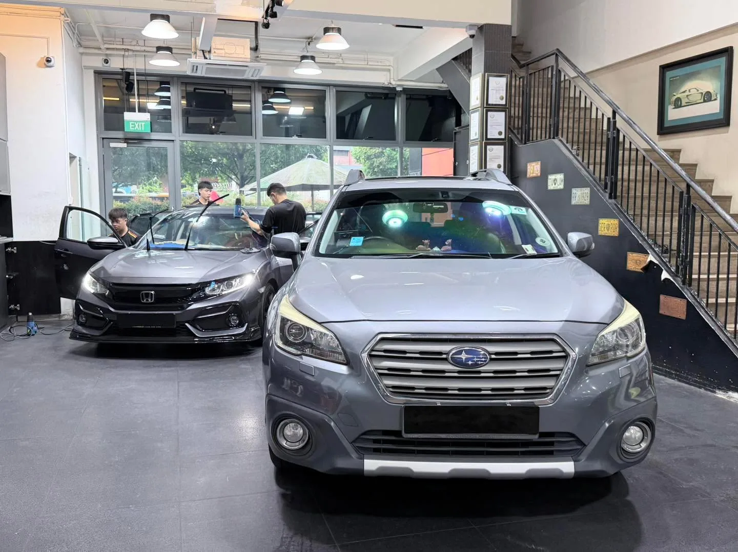 A silver Hyundai Avante sedan and a black Honda sedan in the workshop, viewed from the front.