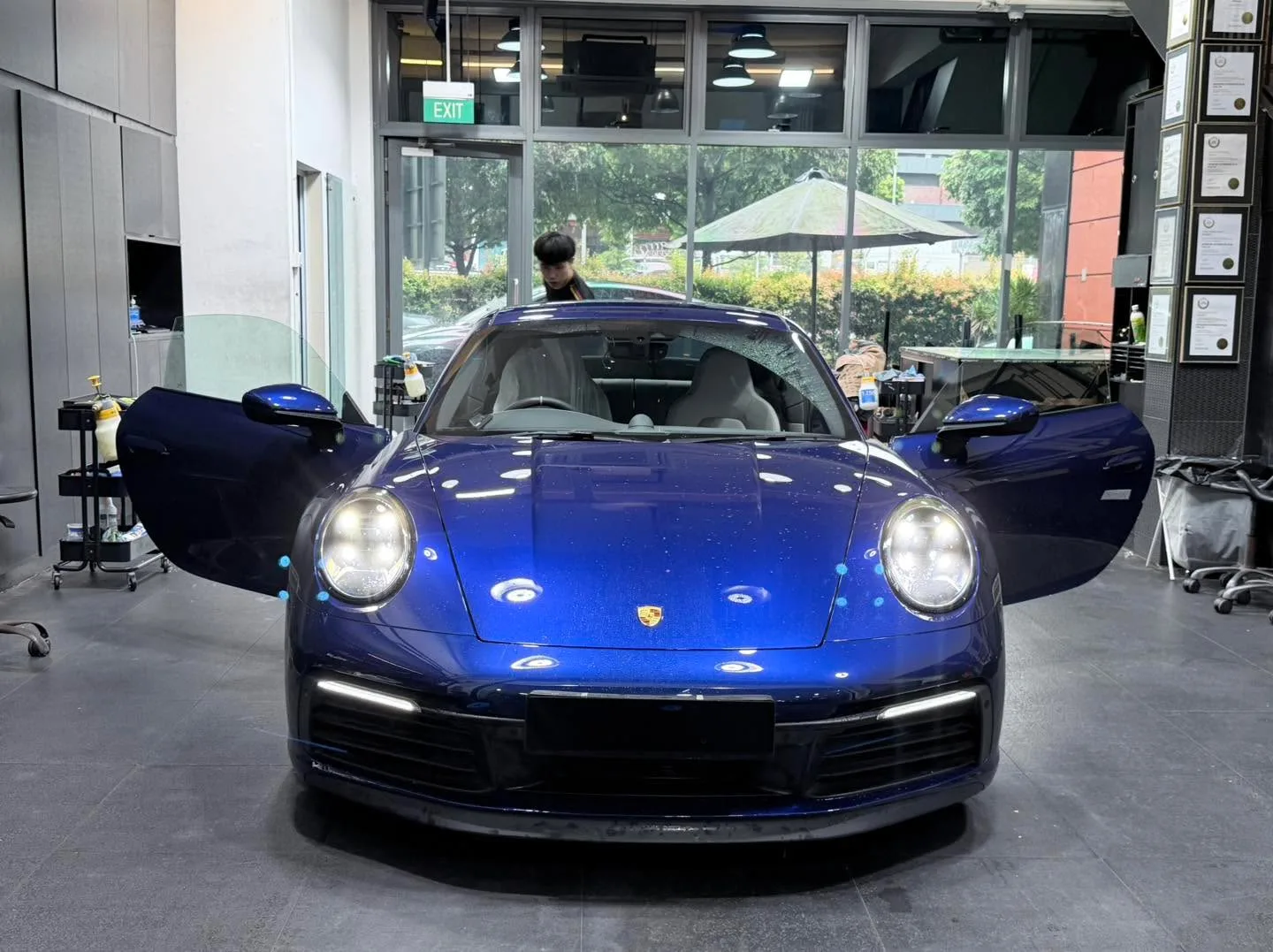 A blue Porsche 911 sports car with both doors open, photographed head-on indoors.
