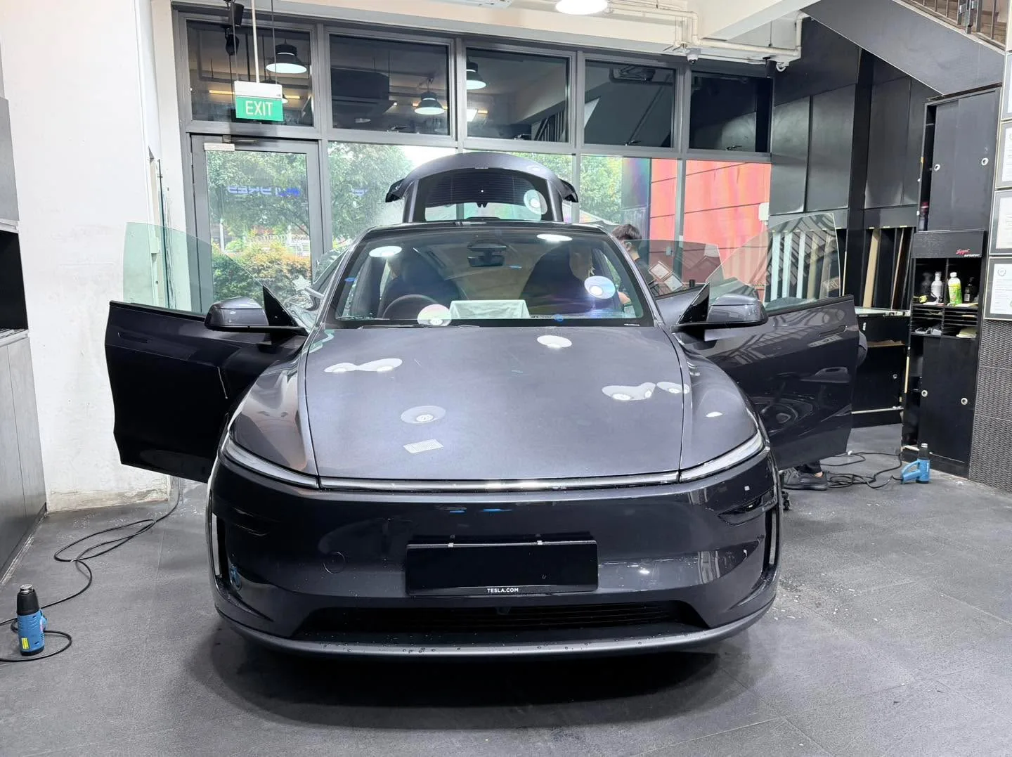 A dark grey Tesla sedan with both falcon doors open, viewed from the front.