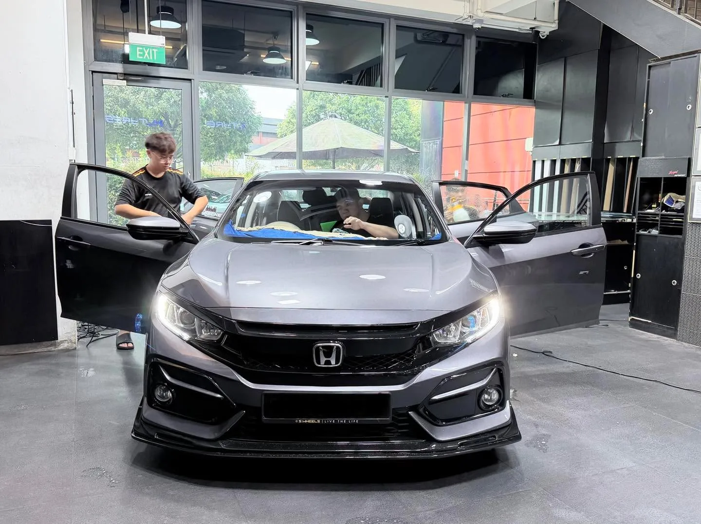 A dark grey Honda sedan with both doors open, viewed from the front indoors.