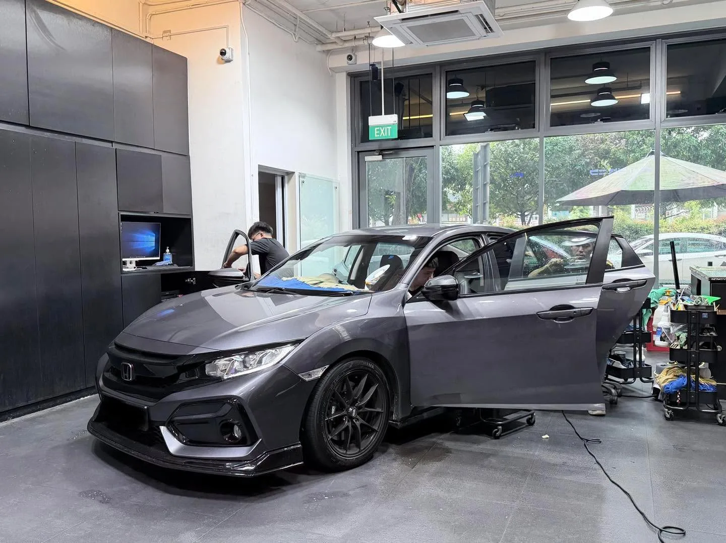 A grey Honda compact car with doors open inside the workshop, photographed from the front.