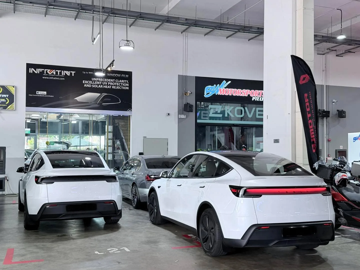 Two white Tesla sedans and a grey car in the Infratint workshop car park.