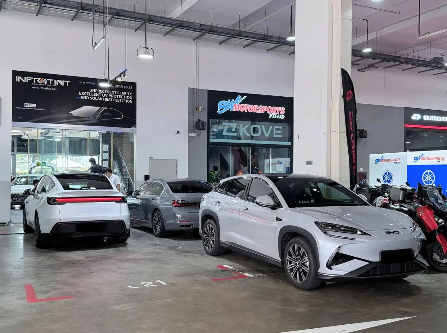 Two white Tesla sedans, a grey car and a dark blue SUV in the Infratint workshop car park.