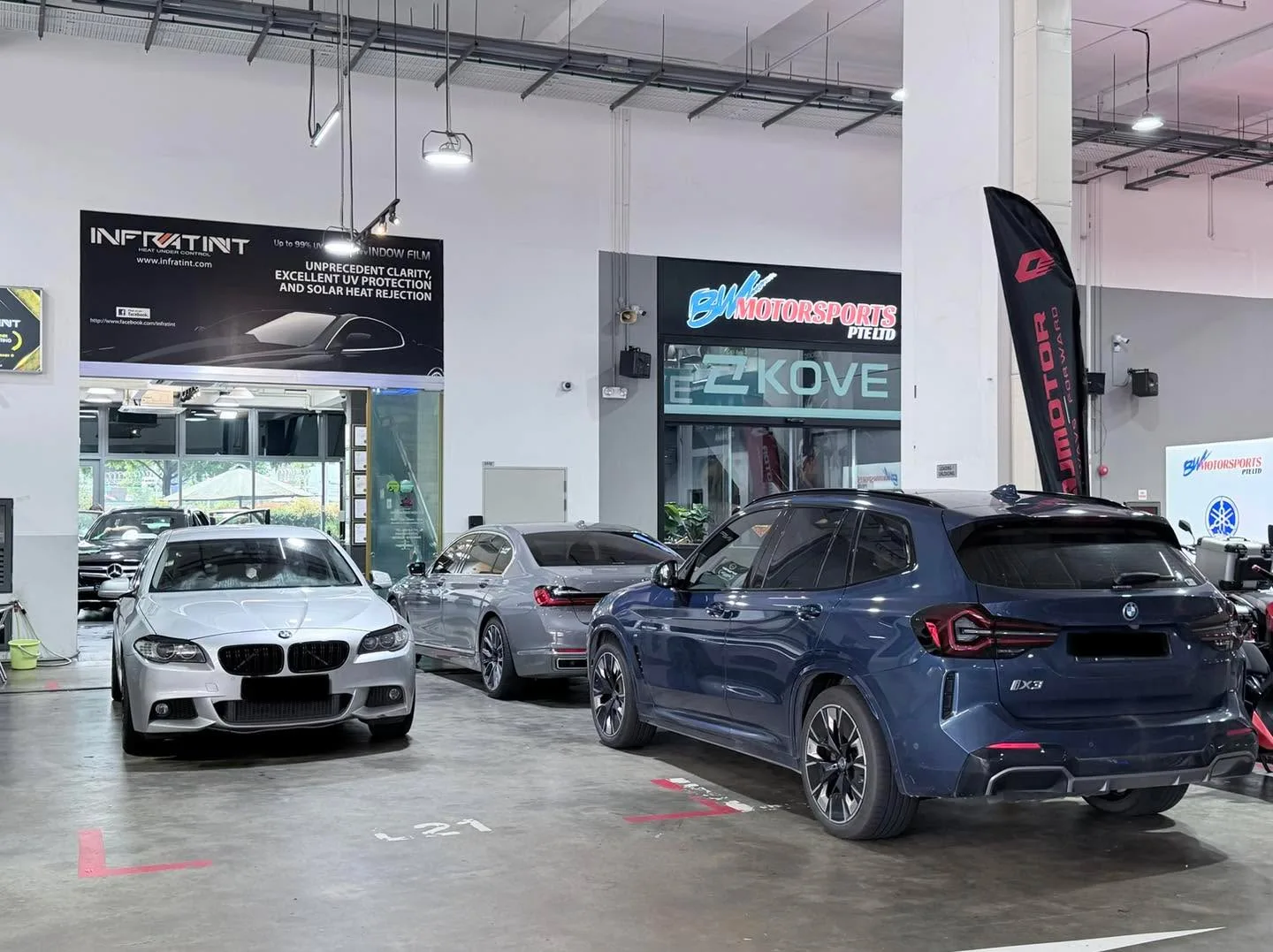 A white Tesla sedan, a white BMW sedan with a dark blue SUV behind it in the Infratint workshop car park.