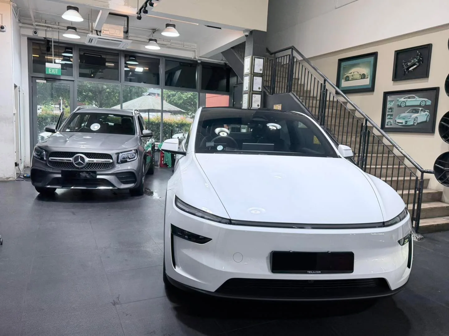 A white Tesla sedan and a black Mercedes-Benz SUV in the workshop.