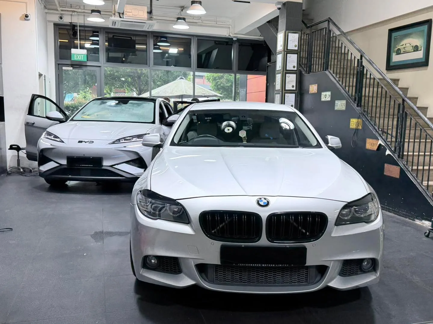 A white BMW sedan and a silver Hyundai hatchback with an open door in the workshop.