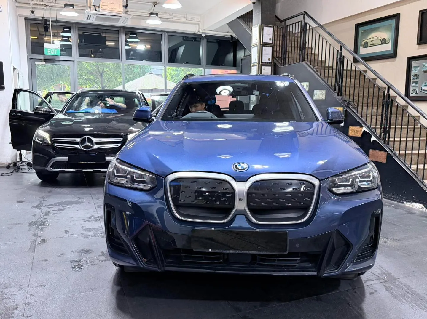 A blue BMW SUV and a black Mercedes-Benz SUV in the workshop.