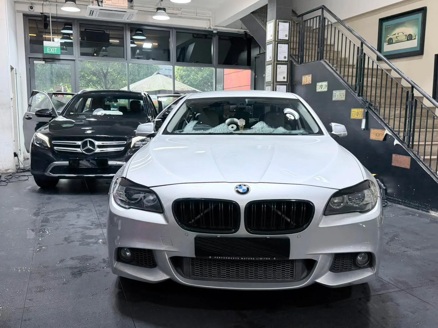 A white BMW sedan and a blue BMW SUV with doors open in the workshop.