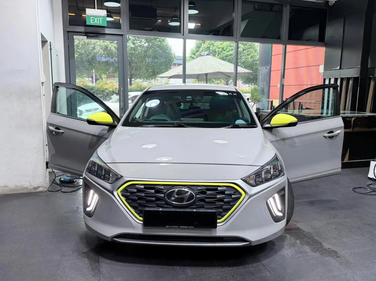 A white Hyundai hatchback with yellow mirror caps and trim and both doors open in the workshop.