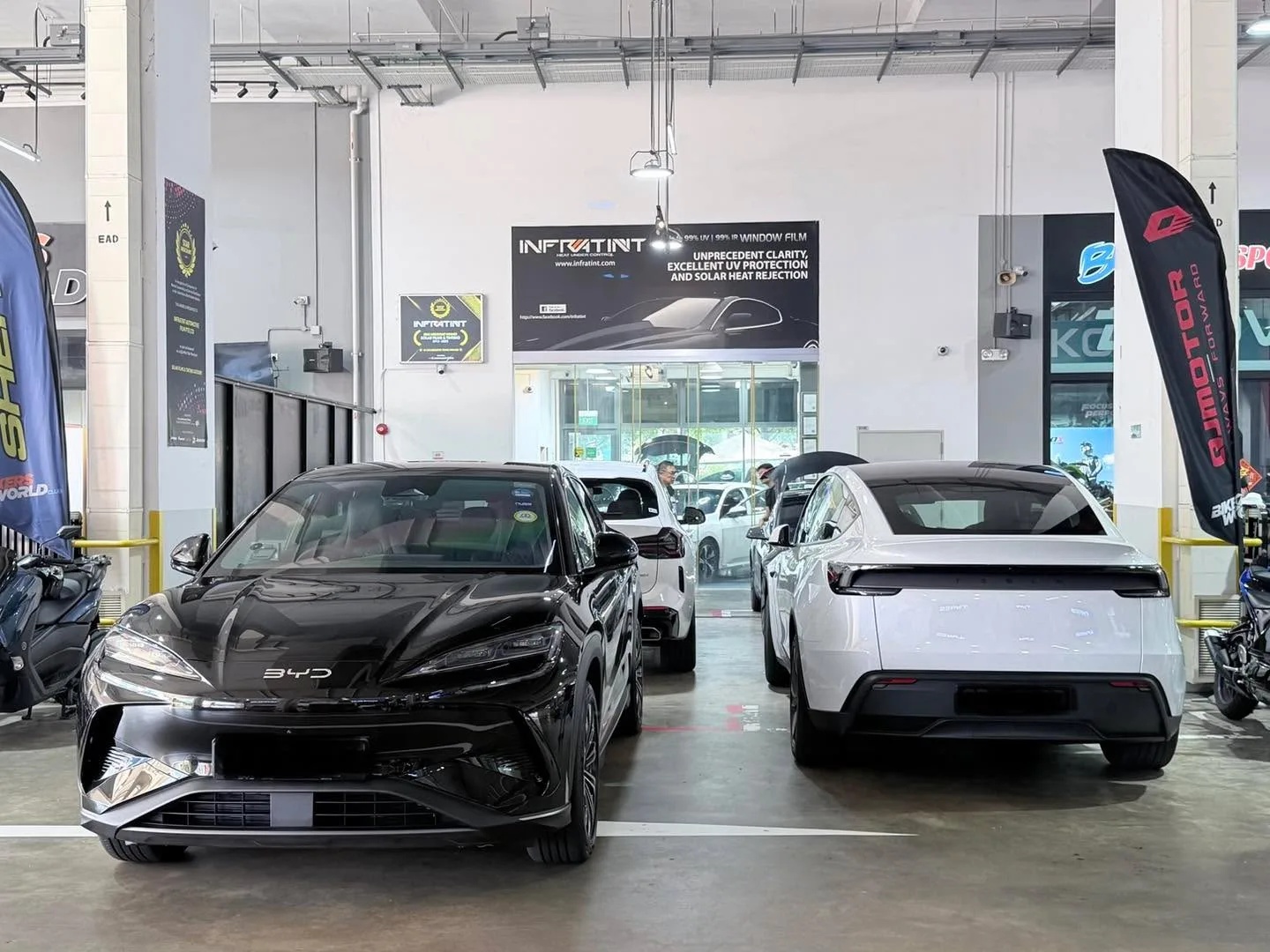 A black Tesla Model Y and a white Tesla sedan parked at the workshop entrance.