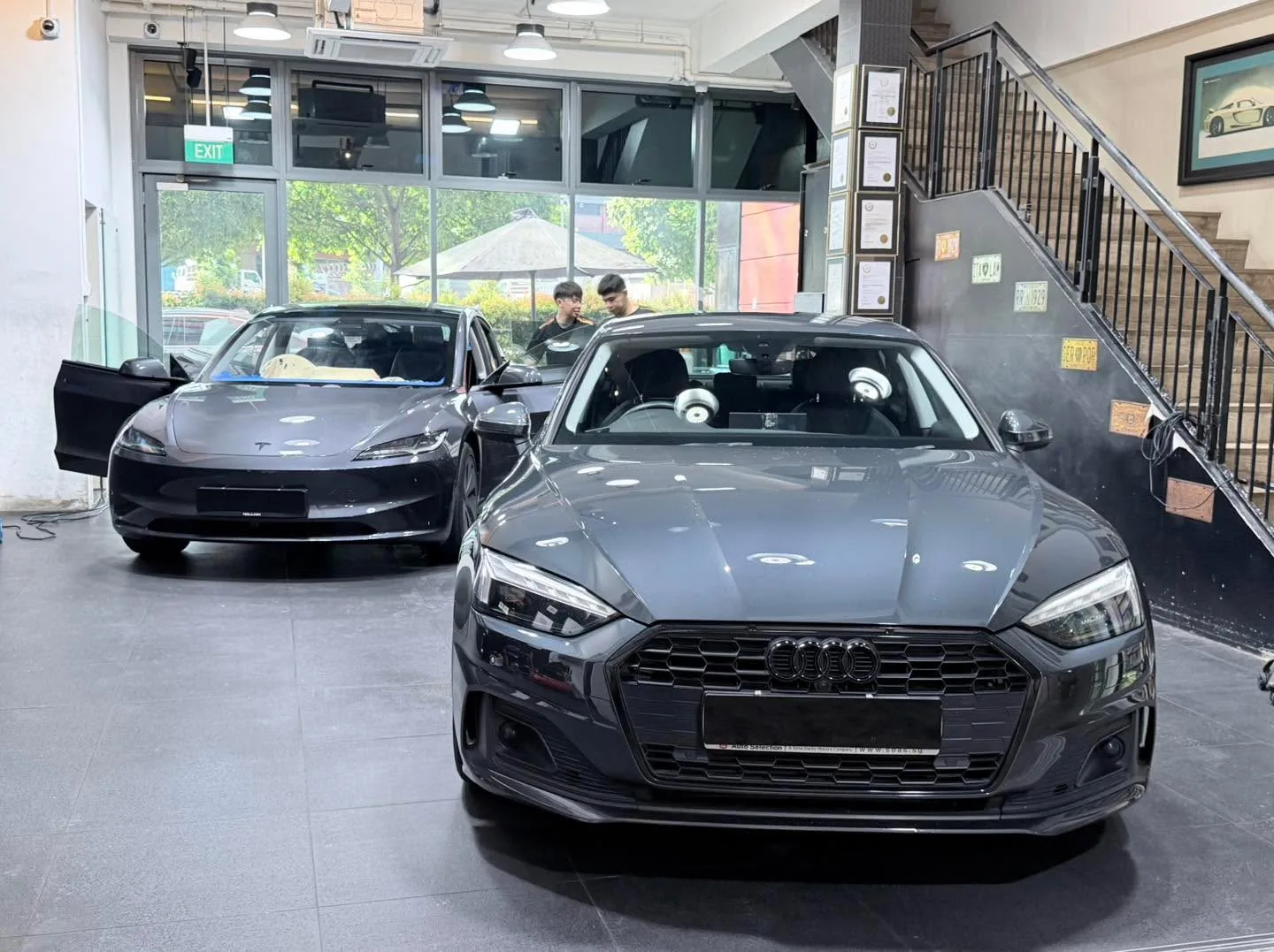 A white Tesla sedan and a black Audi sedan parked front to front indoors.