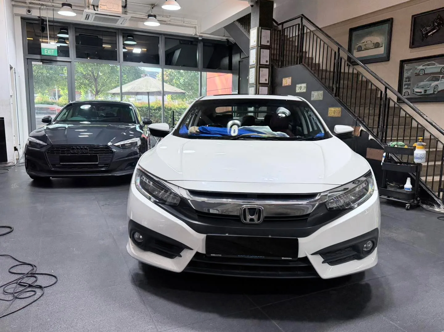A white Honda Civic and a dark-coloured Audi sedan parked indoors with staff working.