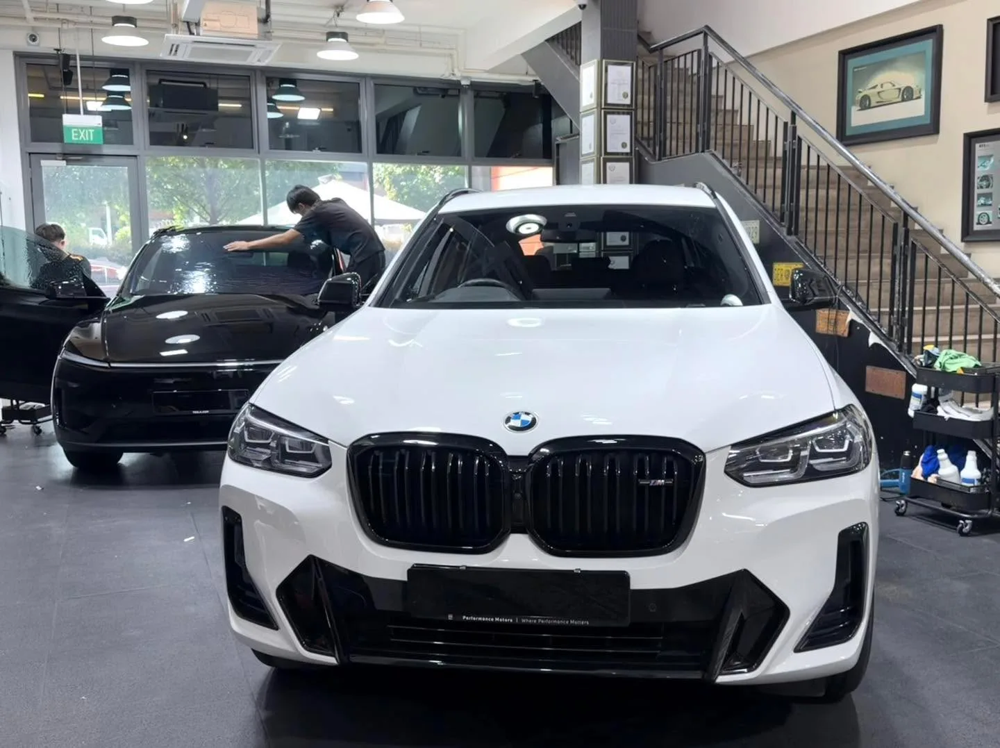 A white BMW SUV and a black sedan parked indoors at the workshop.