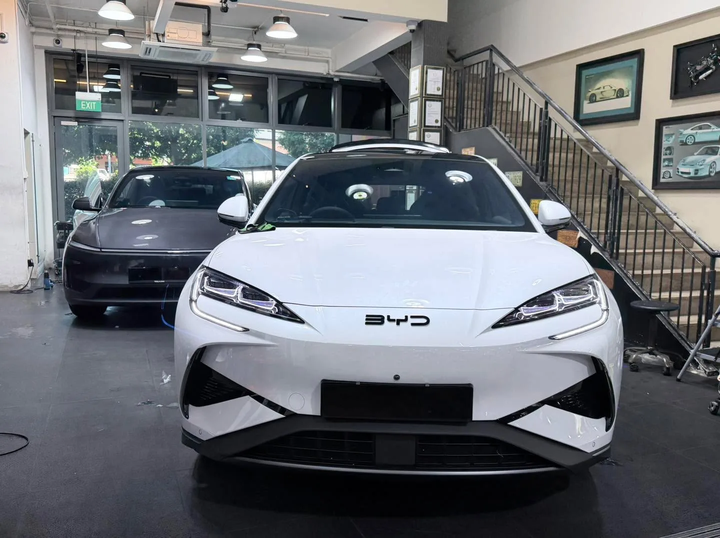 A white Tesla sedan and a dark-coloured sedan parked indoors.