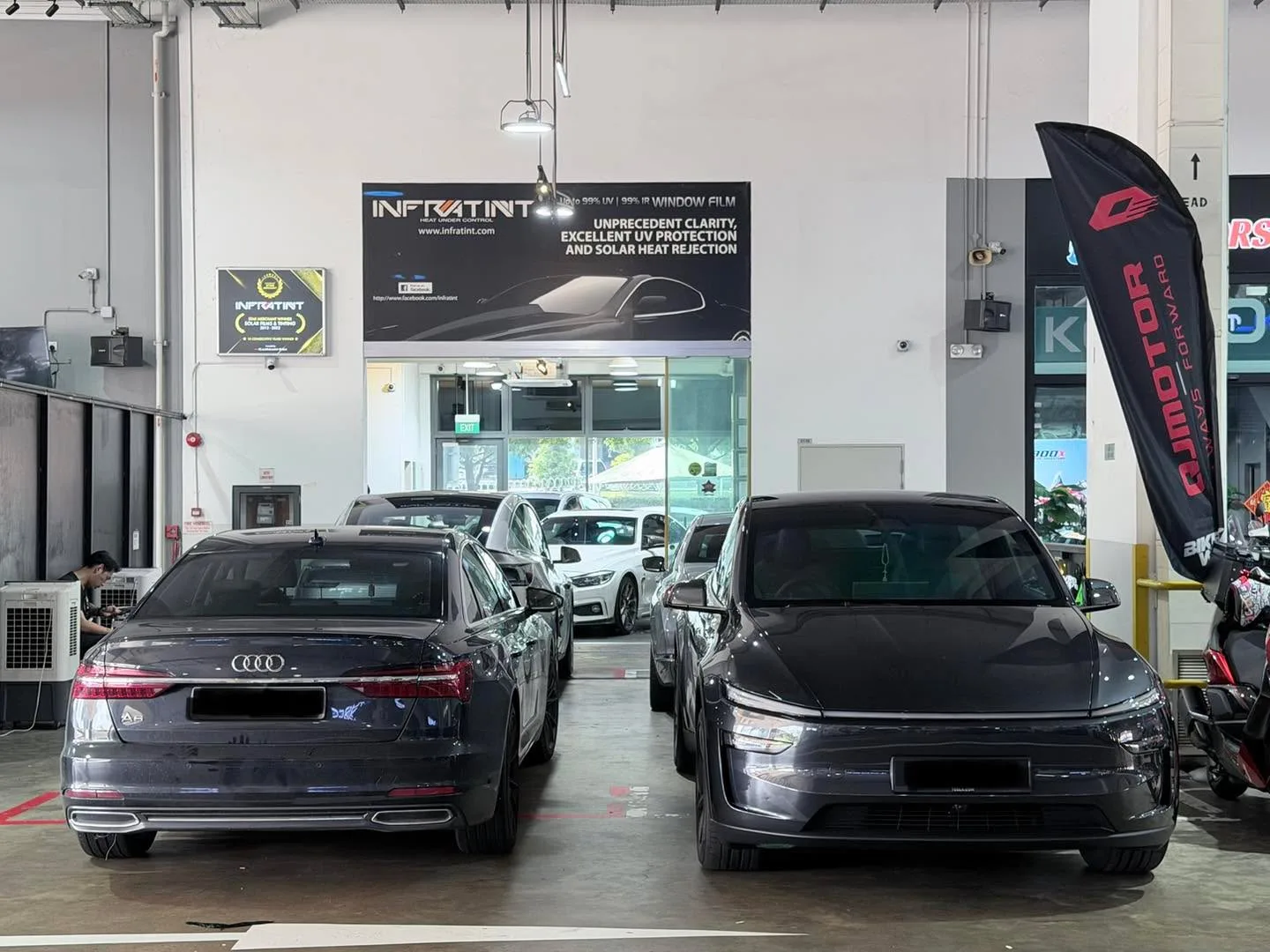 An Audi A6 saloon in dark grey and a dark-coloured car to its left, parked indoors at the workshop.