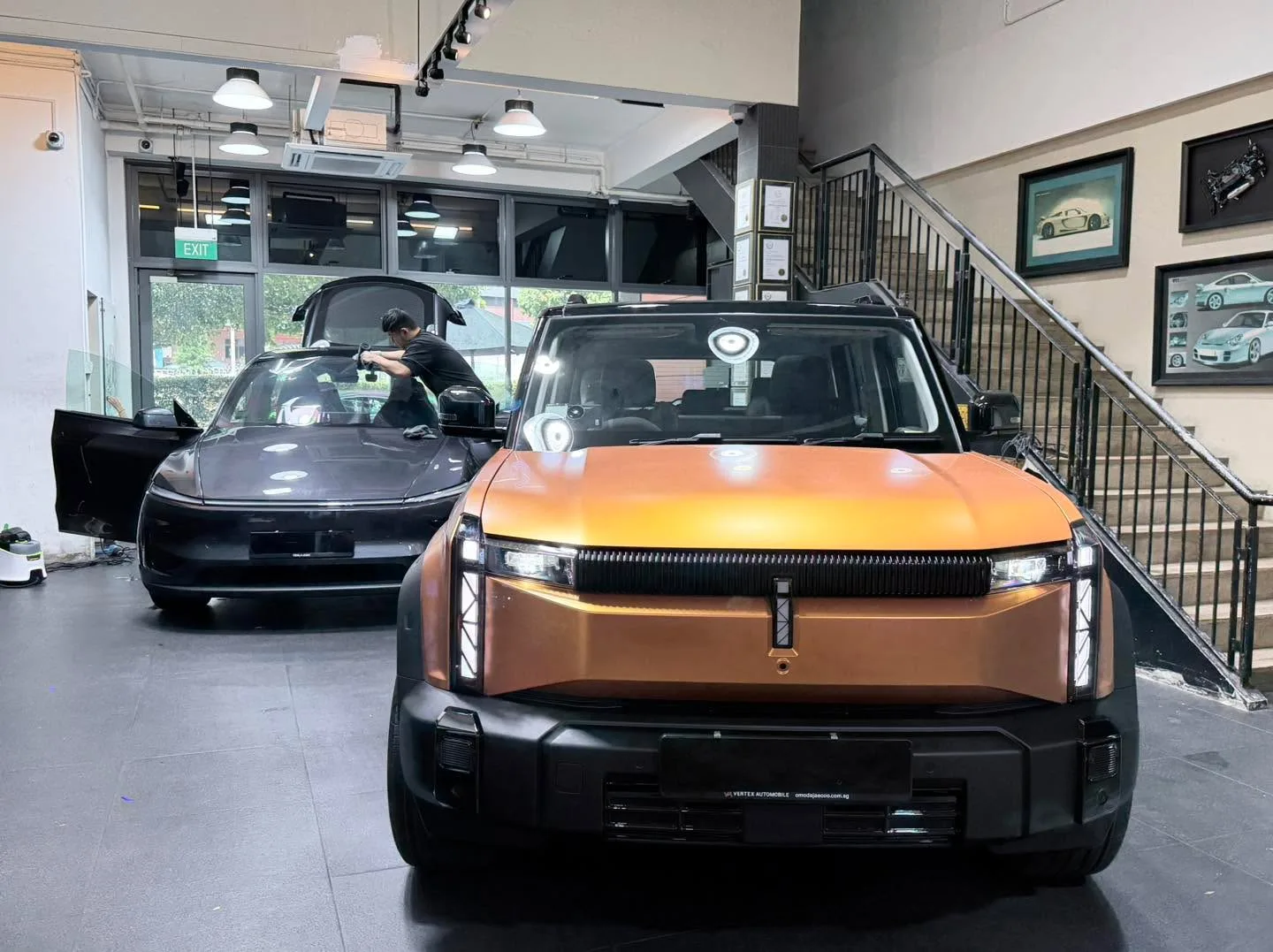 A BYD Sealion 7 in orange and gold gradient and a black Tesla in the background at the workshop.