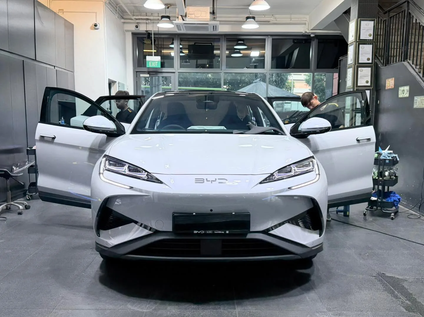 A white BYD sedan with door open in the foreground at the workshop.