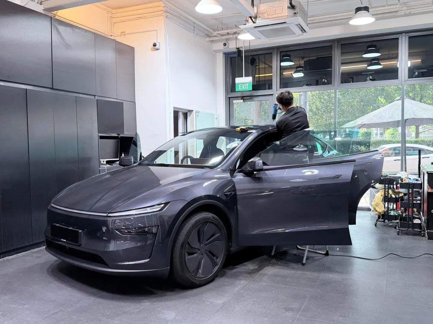 A grey-coloured Xpeng electric saloon with door open, undergoing window tinting work.