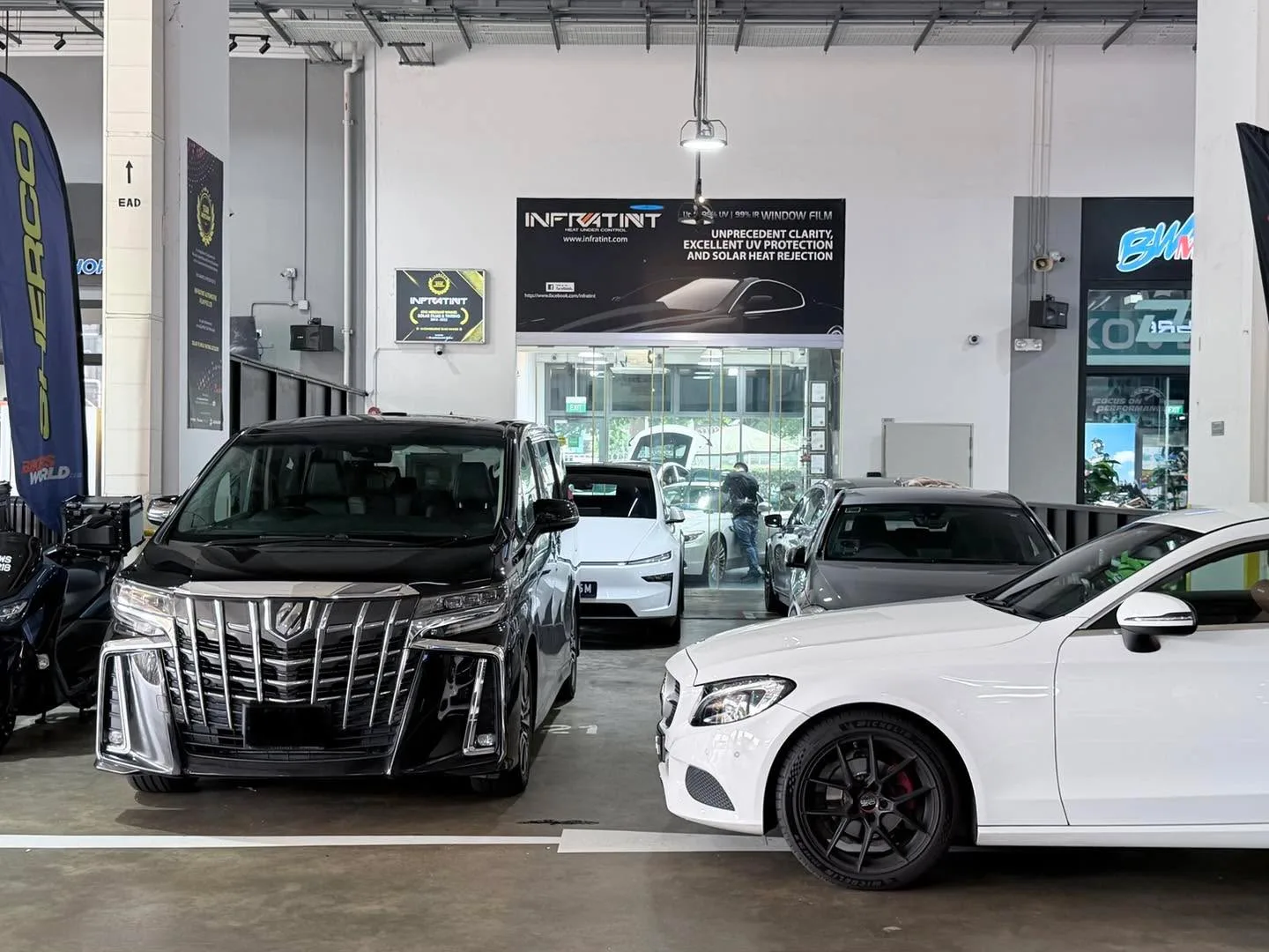 A black Toyota Alphard, a white Mercedes-Benz C-Class coupe, and a dark grey Mercedes-Benz A-Class parked in the workshop.