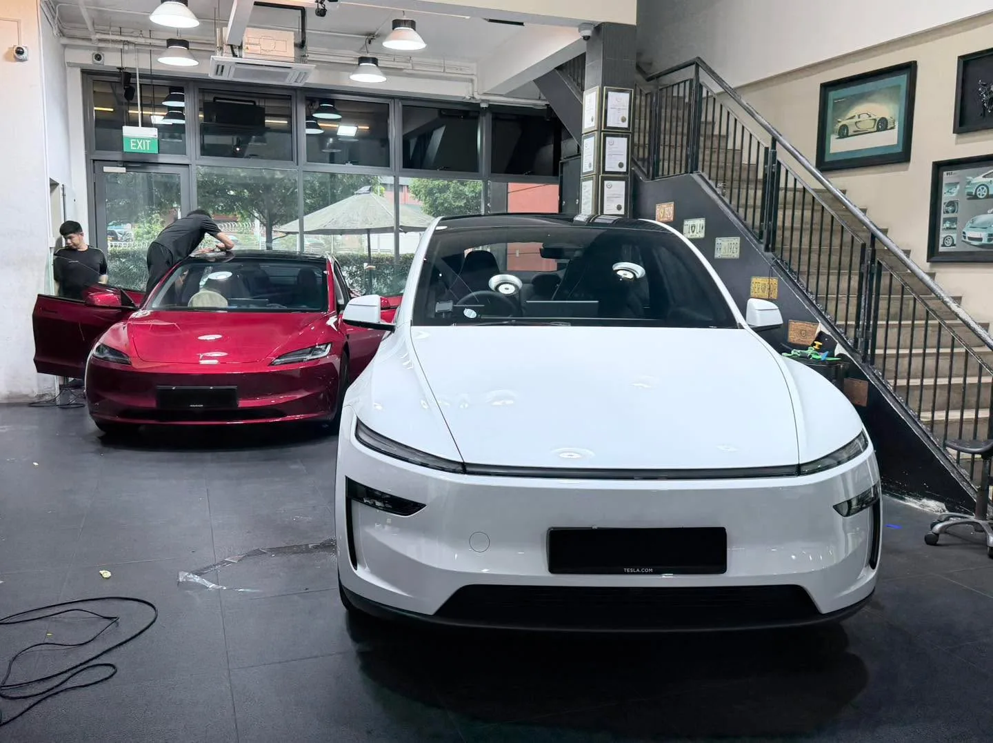 A red Tesla in the foreground and a white Tesla sedan at the workshop interior.