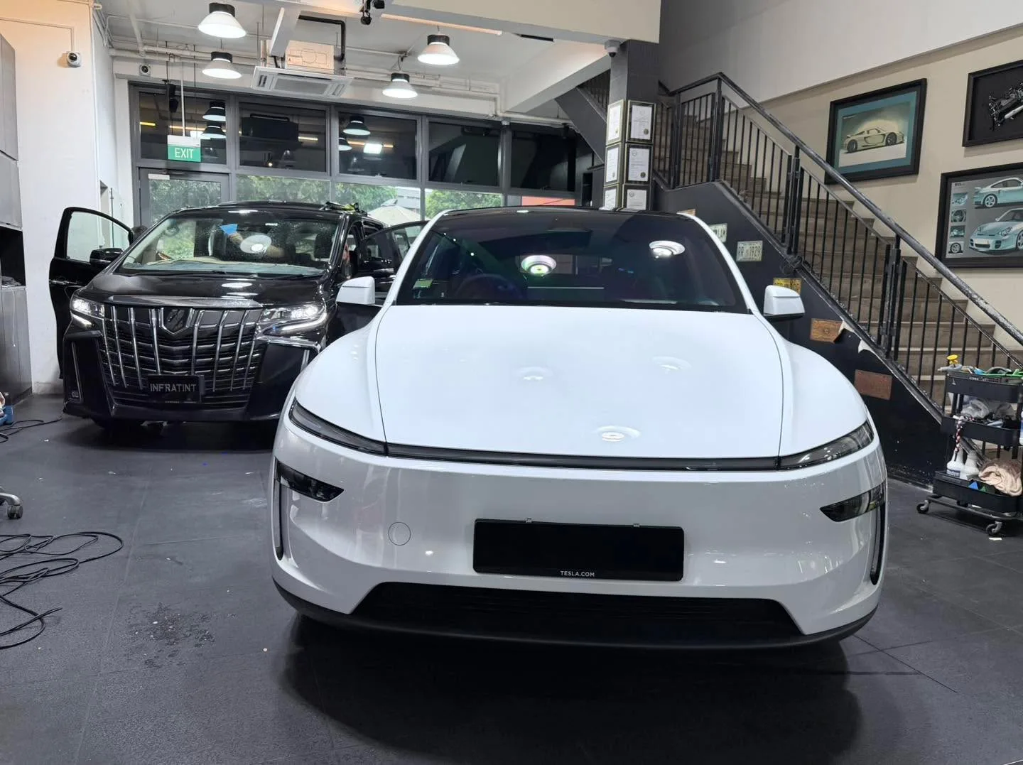 A white Tesla sedan and a black Toyota Alphard parked together in the workshop.