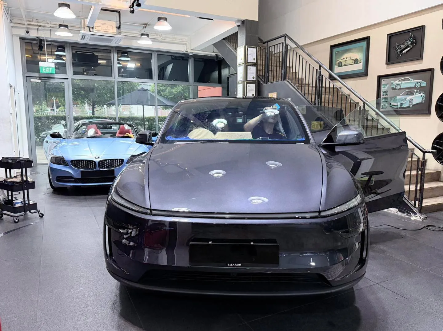 A dark grey Tesla sedan with its door open inside the workshop.