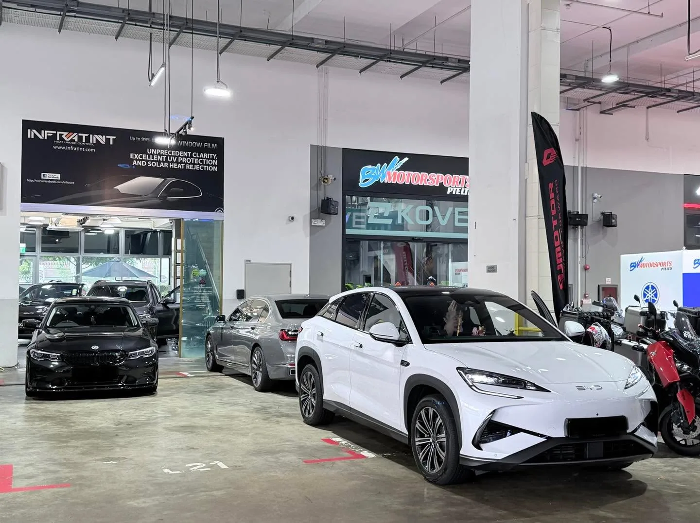 A white BYD Sealing 7 SUV at the workshop, with a black BMW to the left.