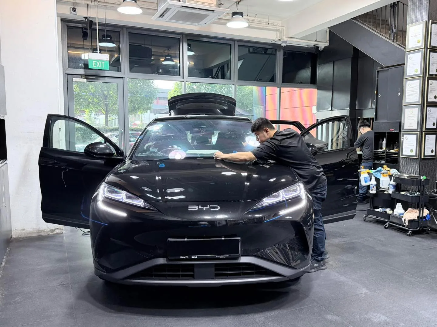 A black BYD Sealing 7 undergoing window film application in the workshop.