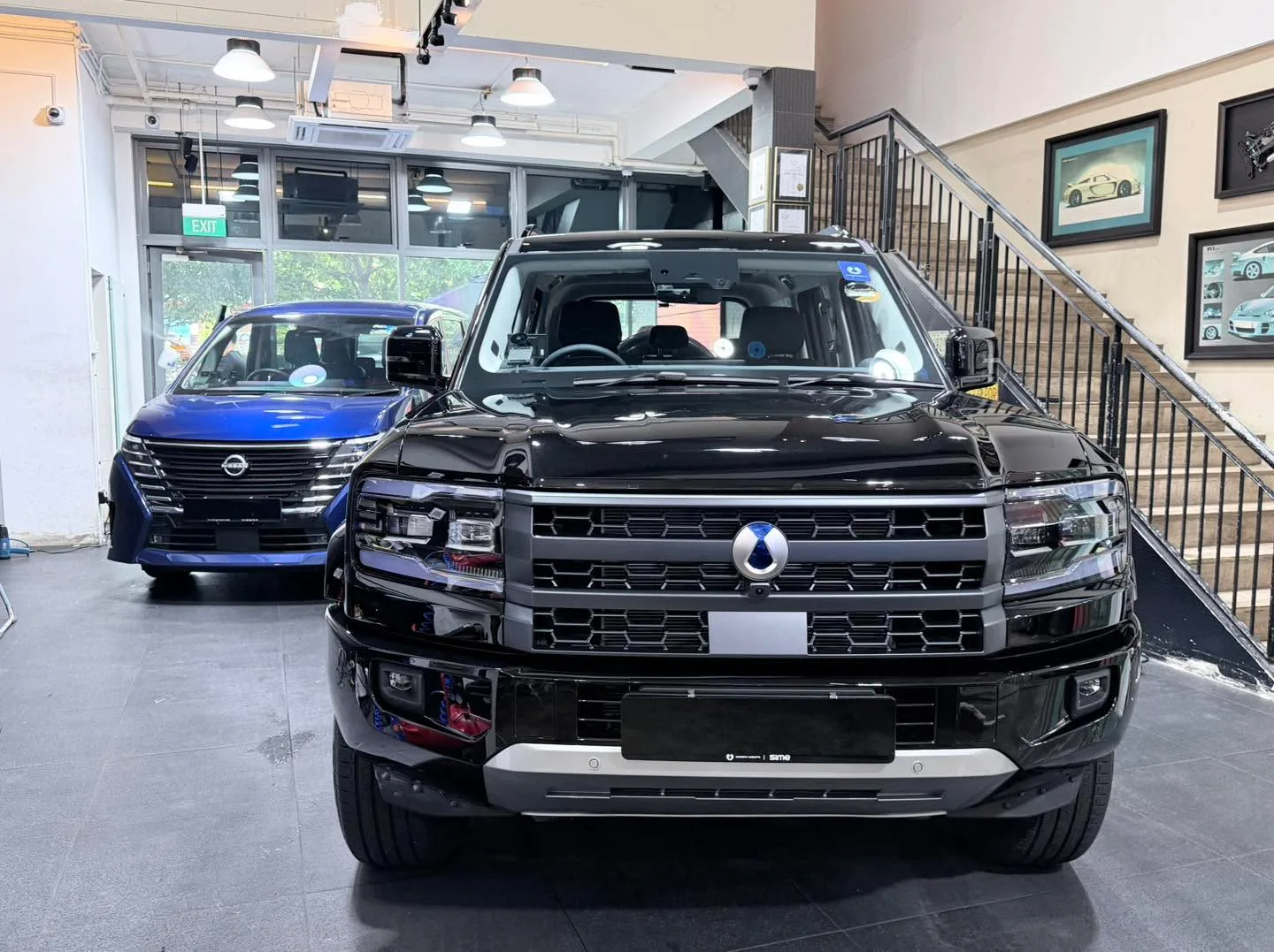 A black full-size SUV with a blue Nissan sedan visible behind it in the workshop.