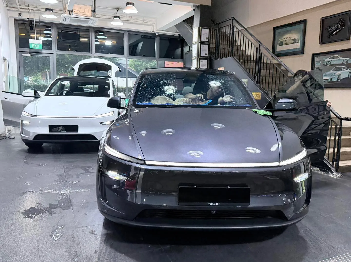 A dark grey Tesla sedan and a white Tesla sedan parked in the workshop.