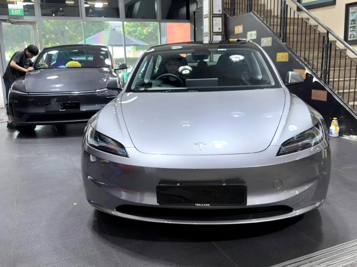 A silver Tesla sedan with technician applying film in the workshop.