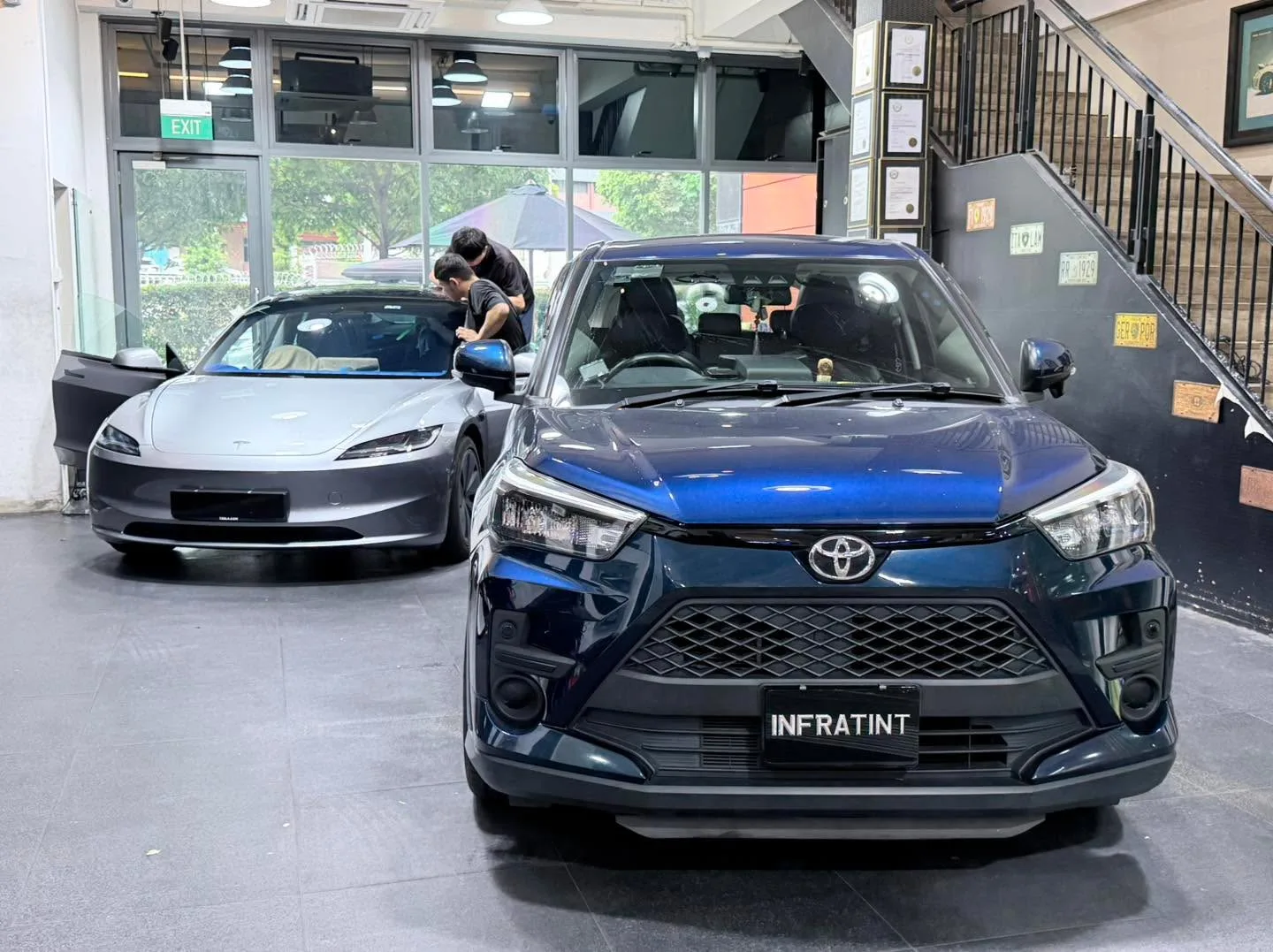 A dark grey Denza sedan and a silver Tesla sedan parked in the workshop.