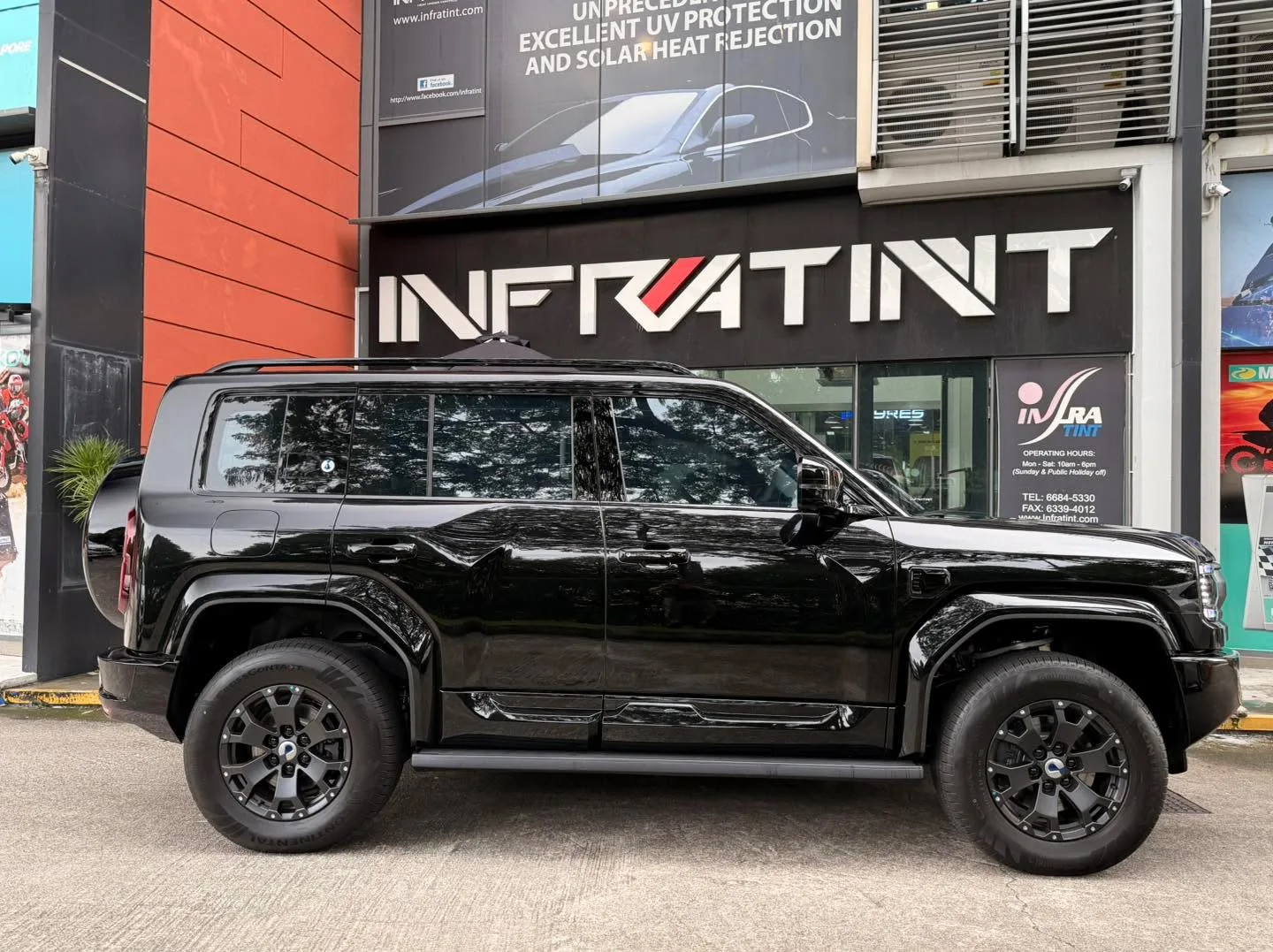 A black Denza B5 SUV parked outside the Infratint storefront, shown from the side.
