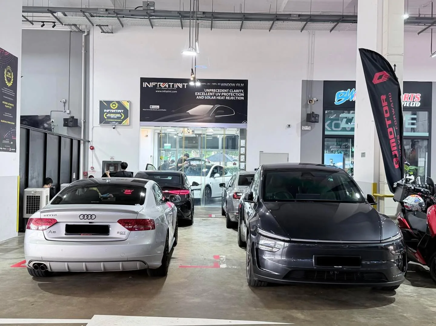 A white Audi A5 sedan and a black saloon in the workshop interior.