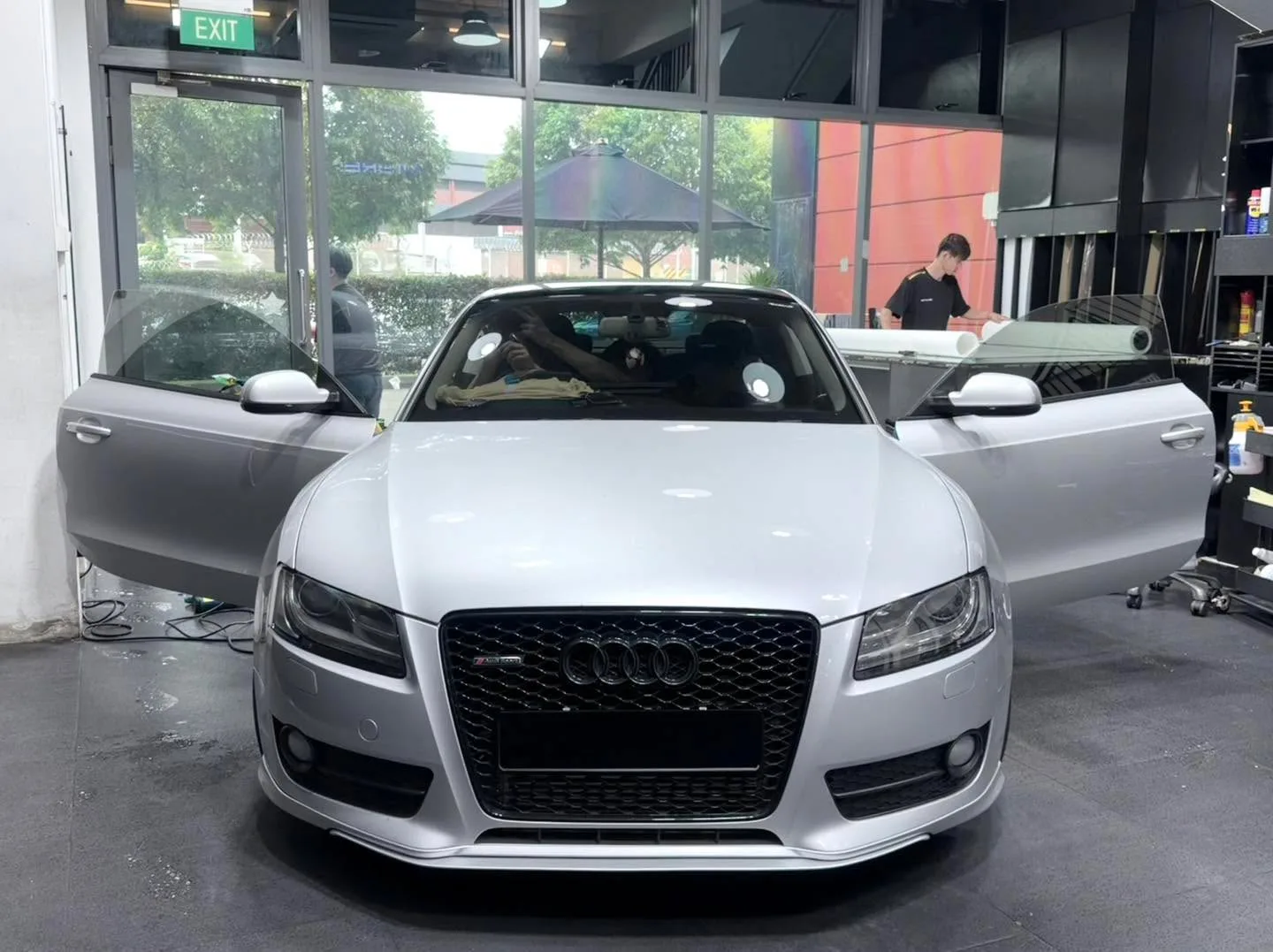 A white Audi A5 coupe with door open, parked next to a grey vehicle inside the workshop.
