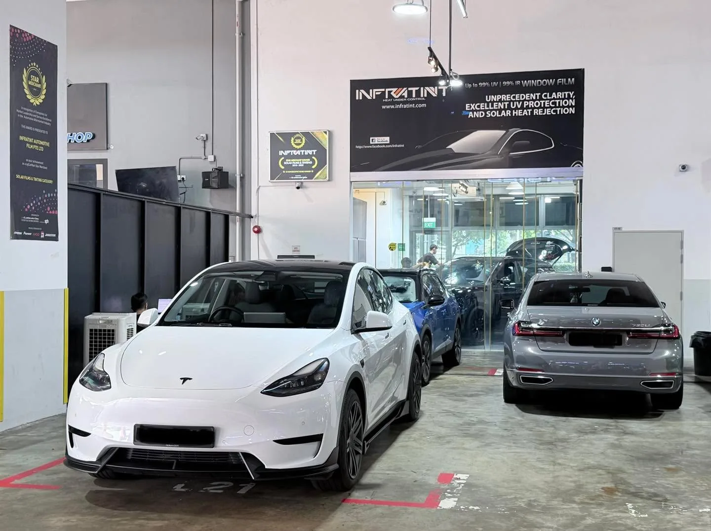 A white Tesla Model Y and blue Zeekr 7X sedan parked in the workshop bay.