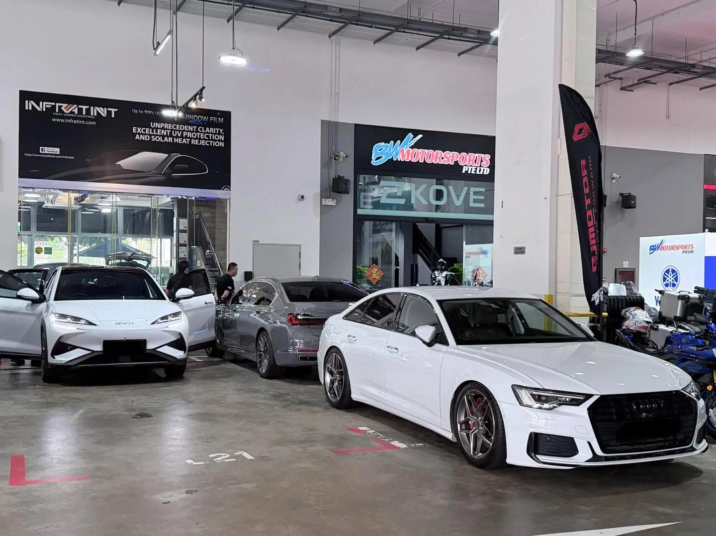 A dark grey Tesla and white Audi A6 saloon parked in the workshop.