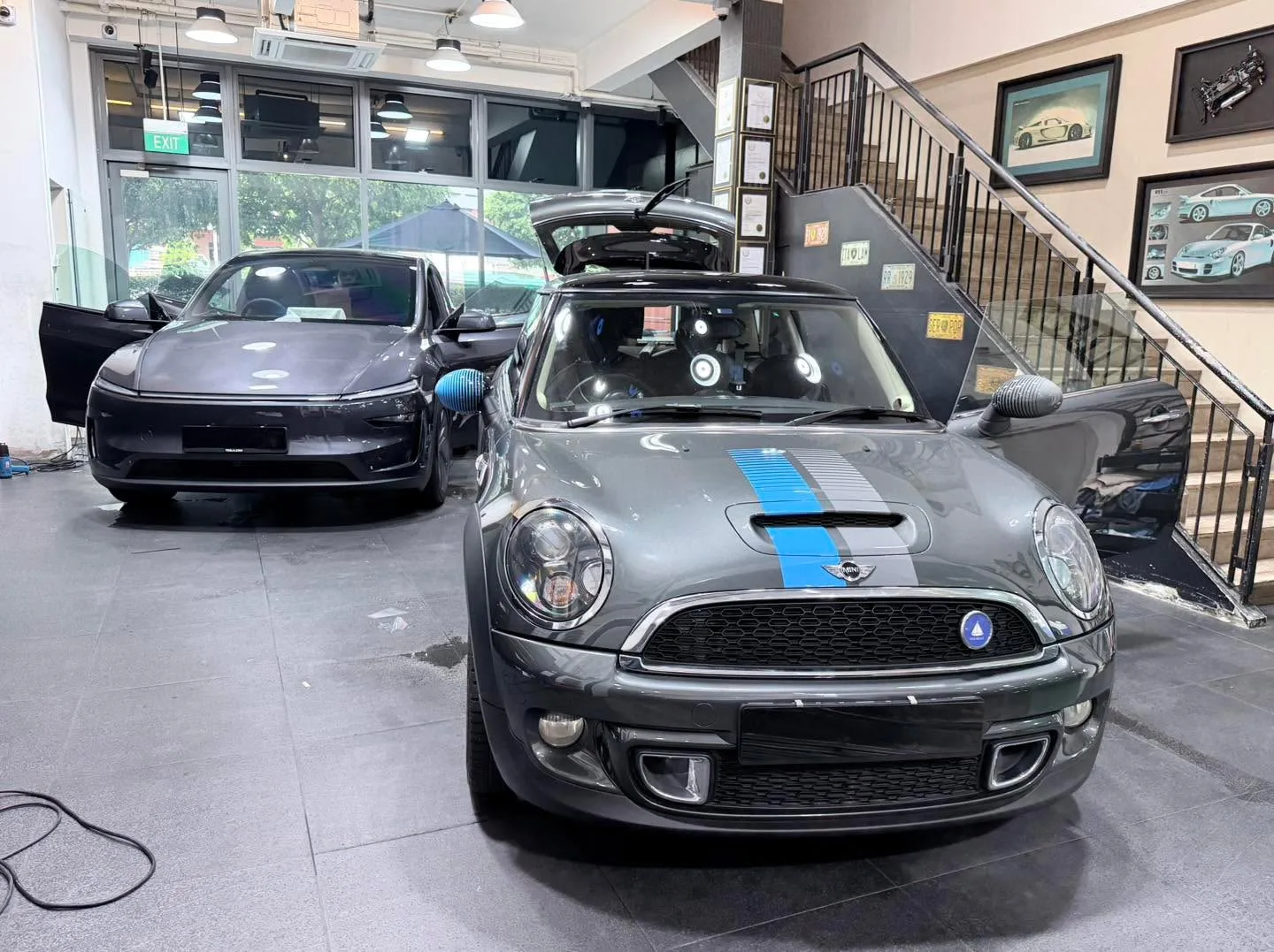 A grey Mini Cooper S with blue racing stripes parked indoors.