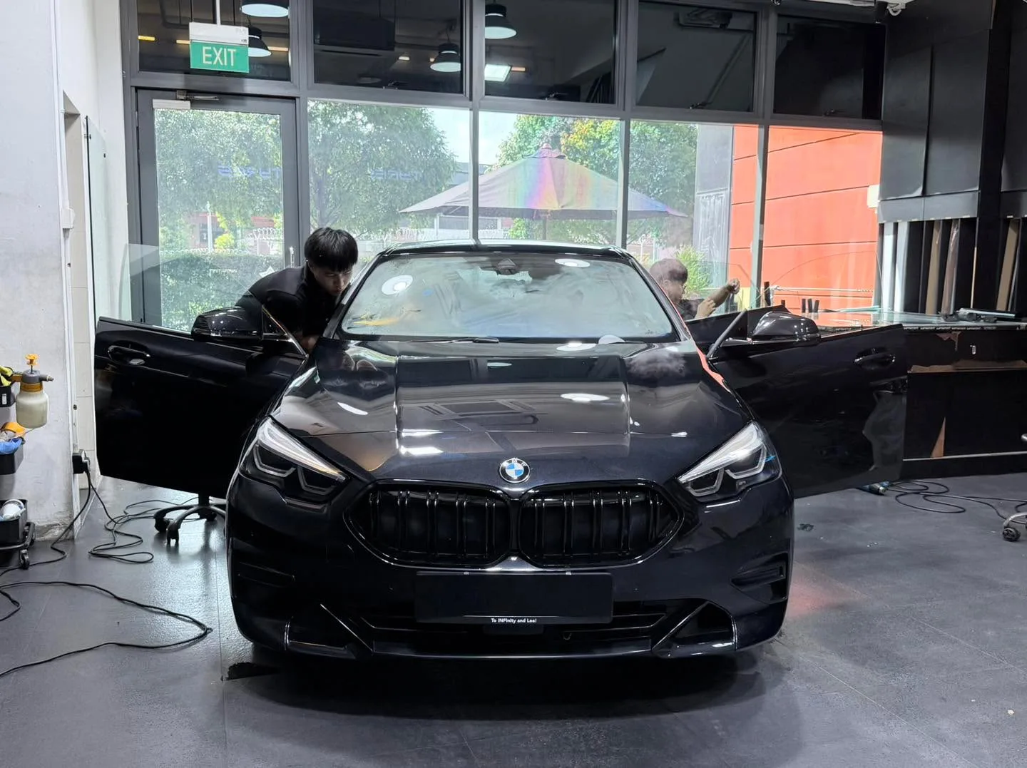 A black BMW sedan undergoing window tinting with staff working on it.