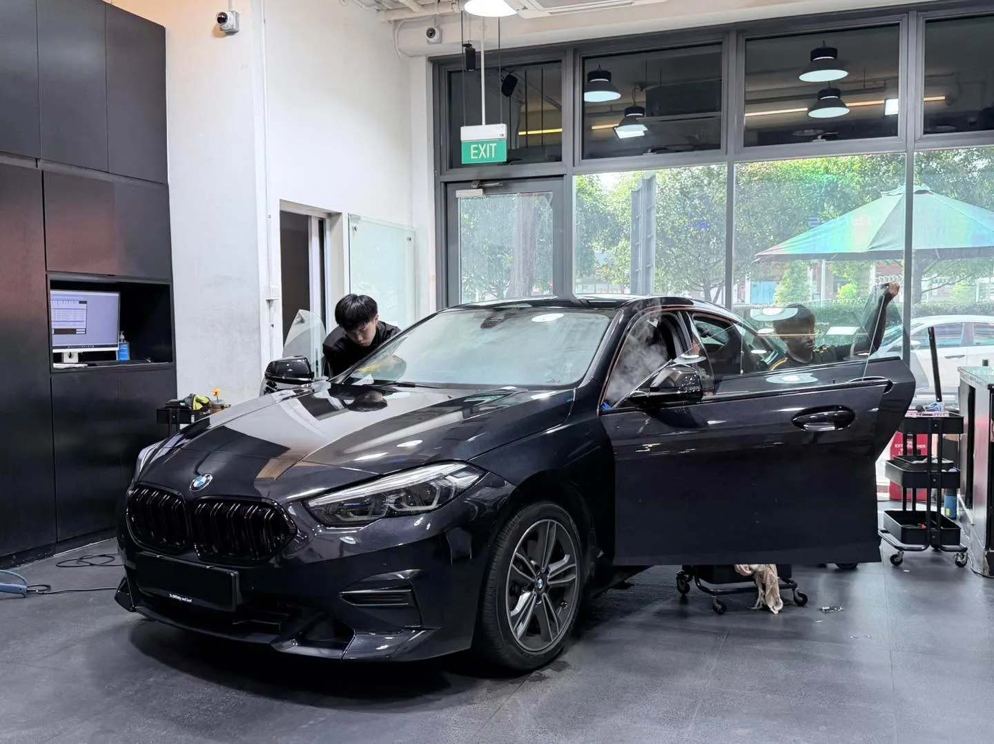 A black BMW sedan parked indoors with doors open during tinting work.