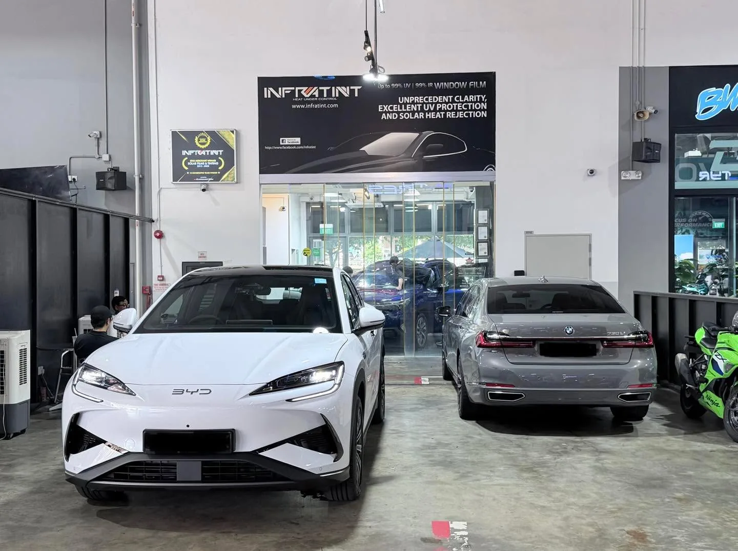 A white BYD Sealing 7 electric SUV and a silver BMW saloon parked indoors.