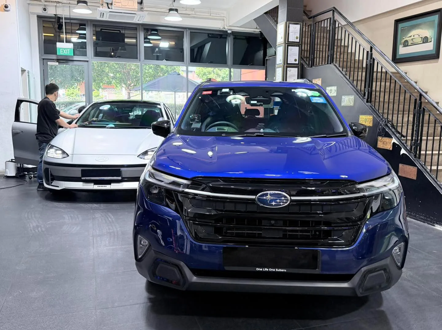 A grey Mercedes-Benz GLC SUV and white BYD Sealing 7 SUV in the workshop with technicians.