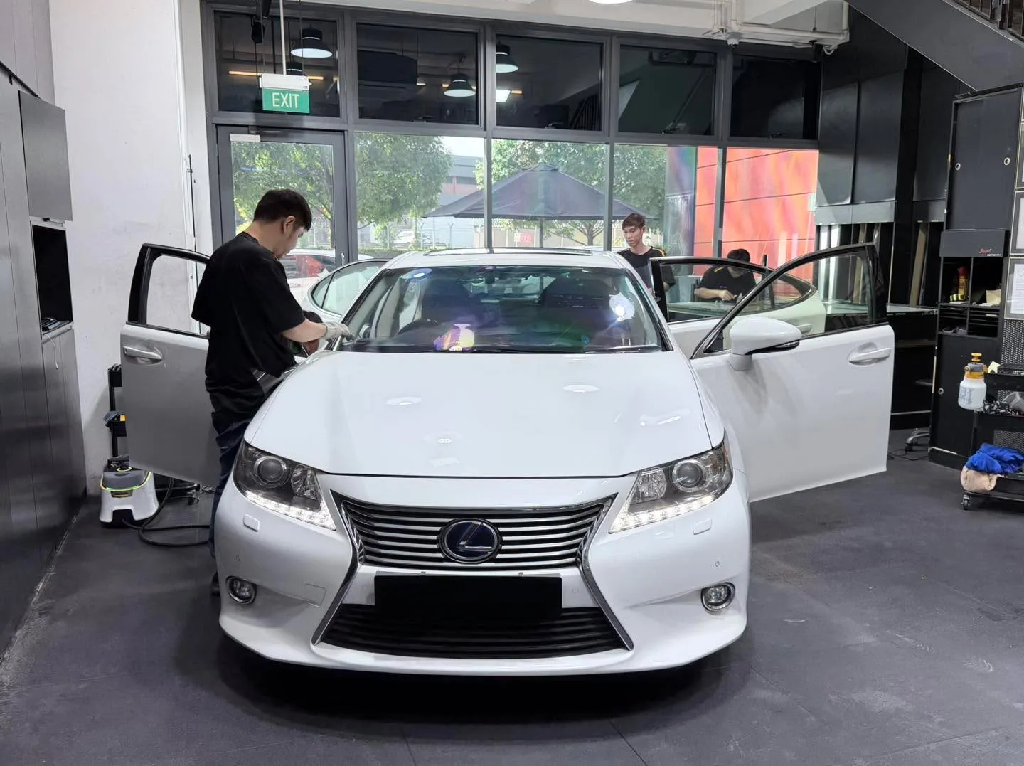 A burgundy Nissan Pulsar saloon and black Tesla sedan inside the workshop with technicians working.