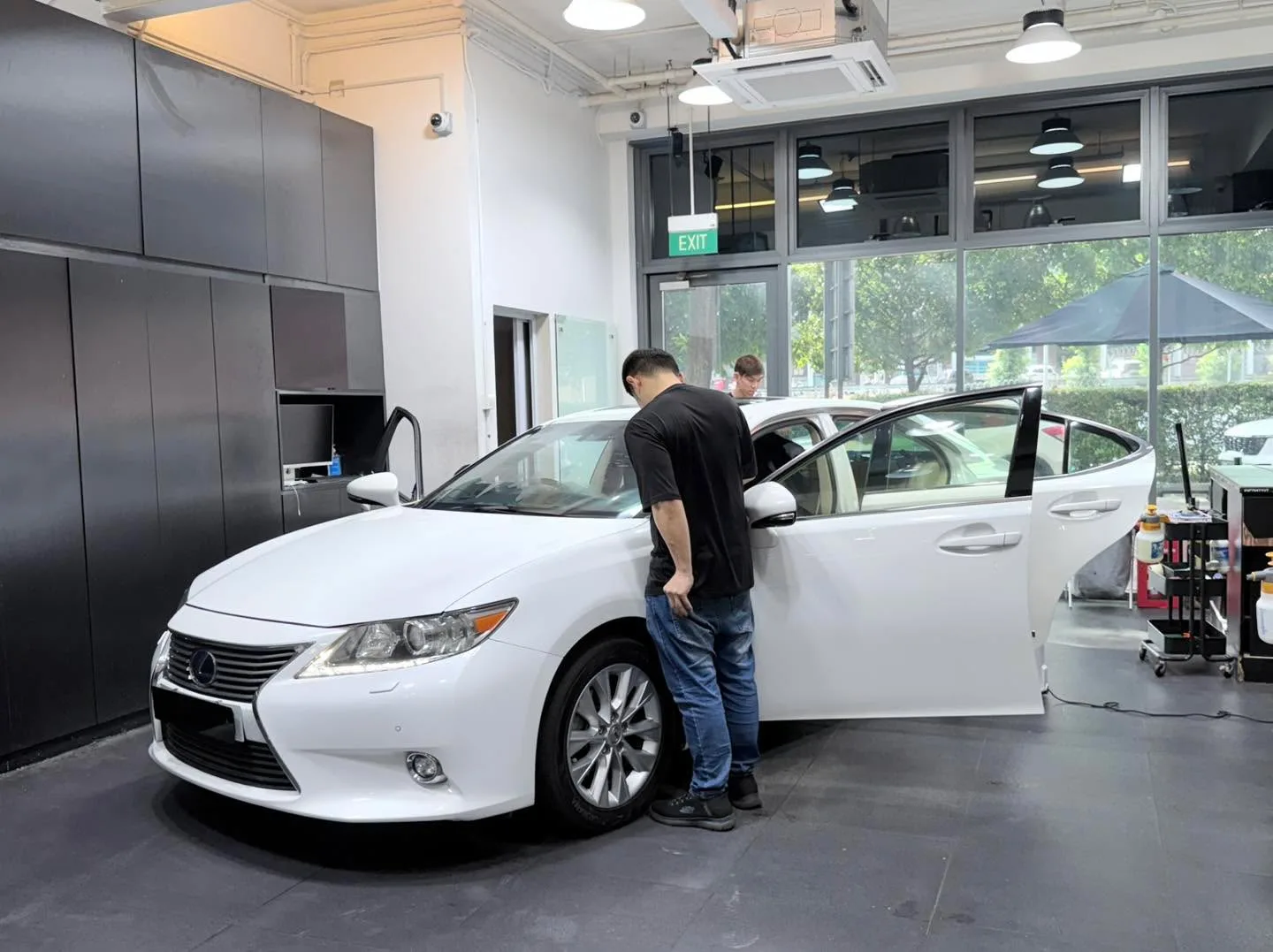 A white Lexus ES300h saloon with doors open, technician applying window film indoors.