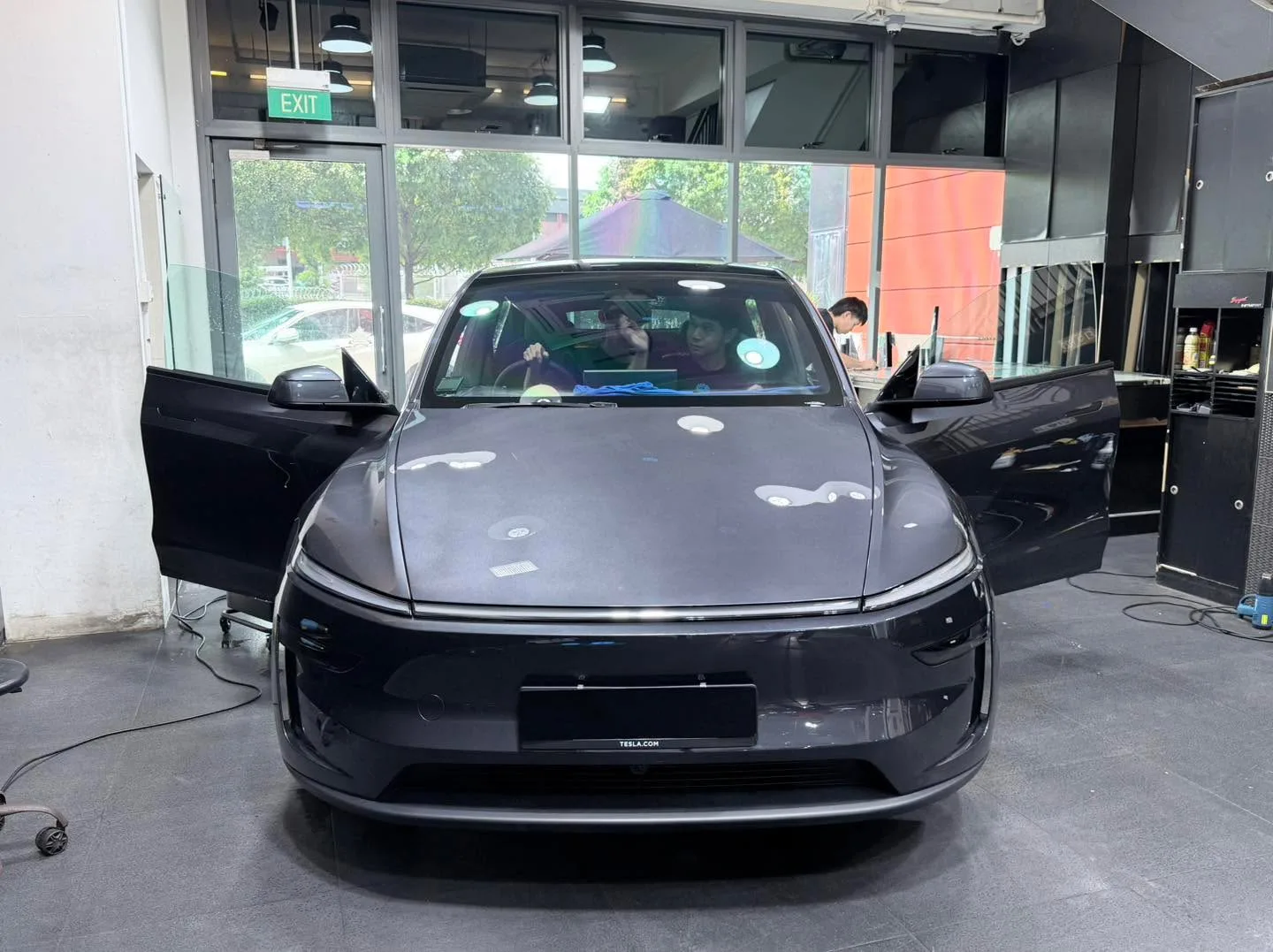A black Tesla sedan with gull-wing doors open facing the camera indoors.