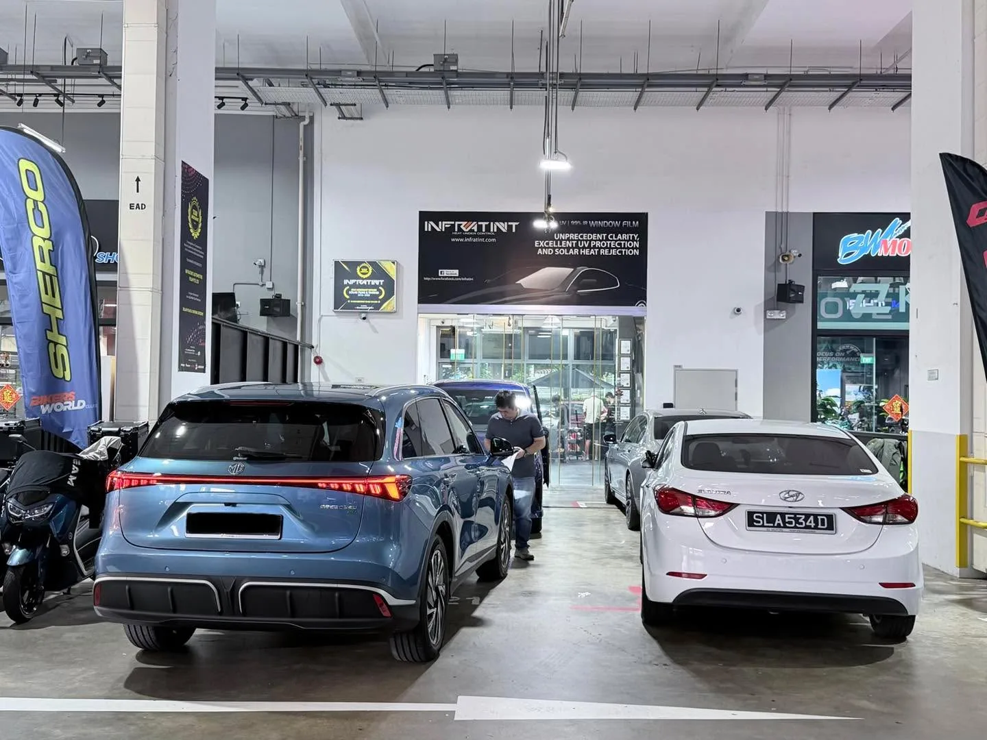 A blue electric crossover and a white sedan parked in the workshop.