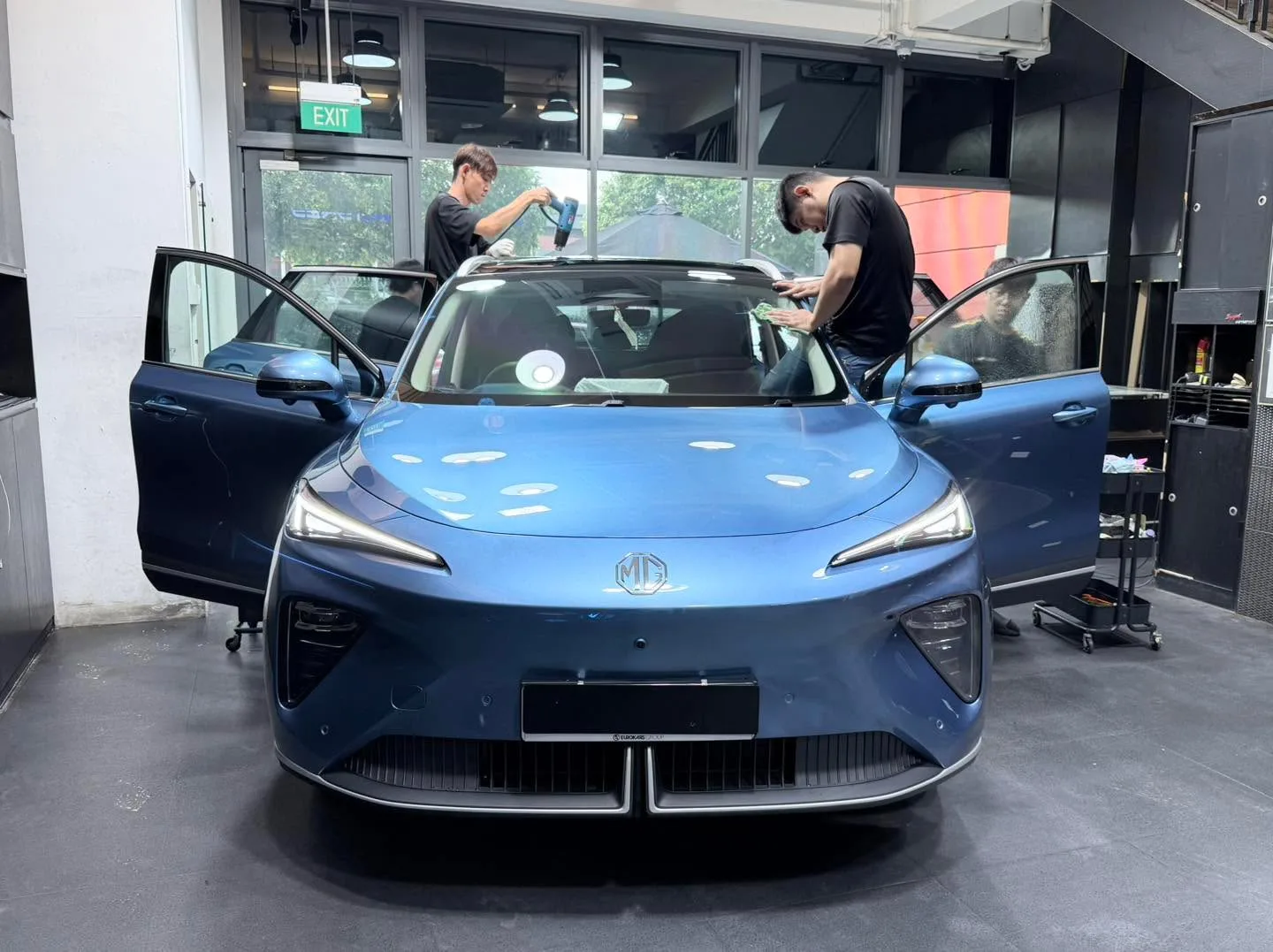 A blue Zeekr 7X with doors open whilst technicians work on the windscreen.