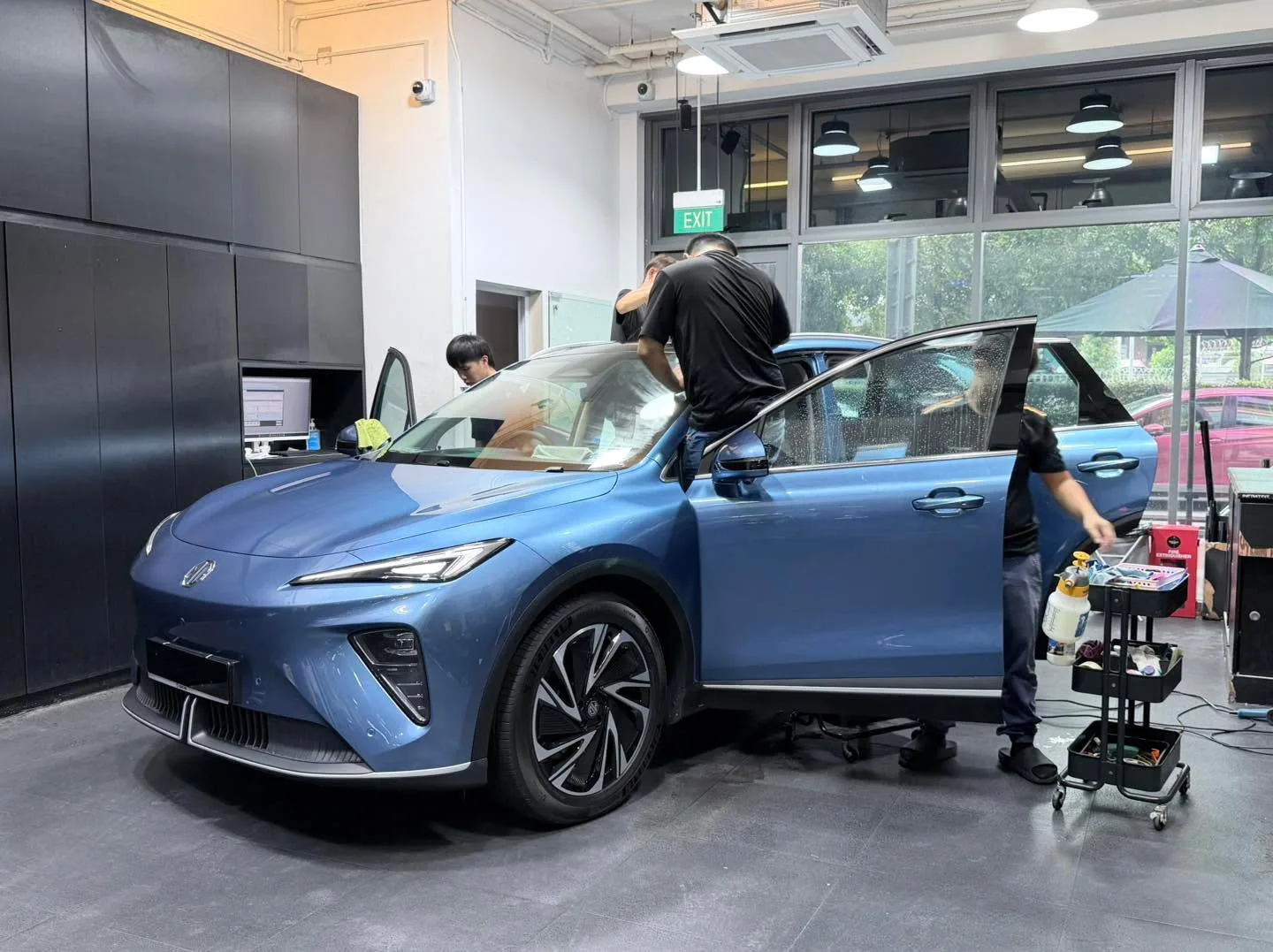 A blue Zeekr 7X with doors open during tinting work.